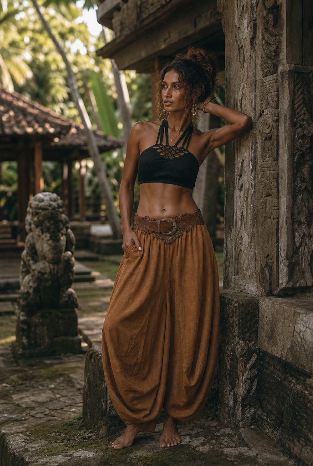 A woman posing outdoors in a tropical setting, wearing a black halter crop top and a brown wide-leg harem pant set with a matching belt.