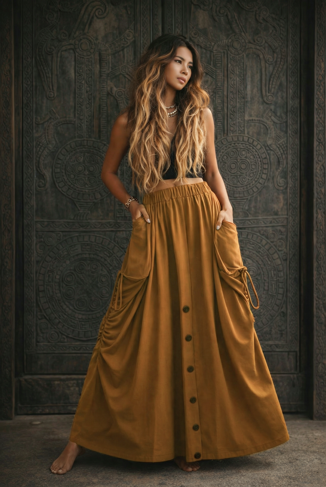 Woman wearing a long mustard yellow skirt with buttons against a dark textured wall.