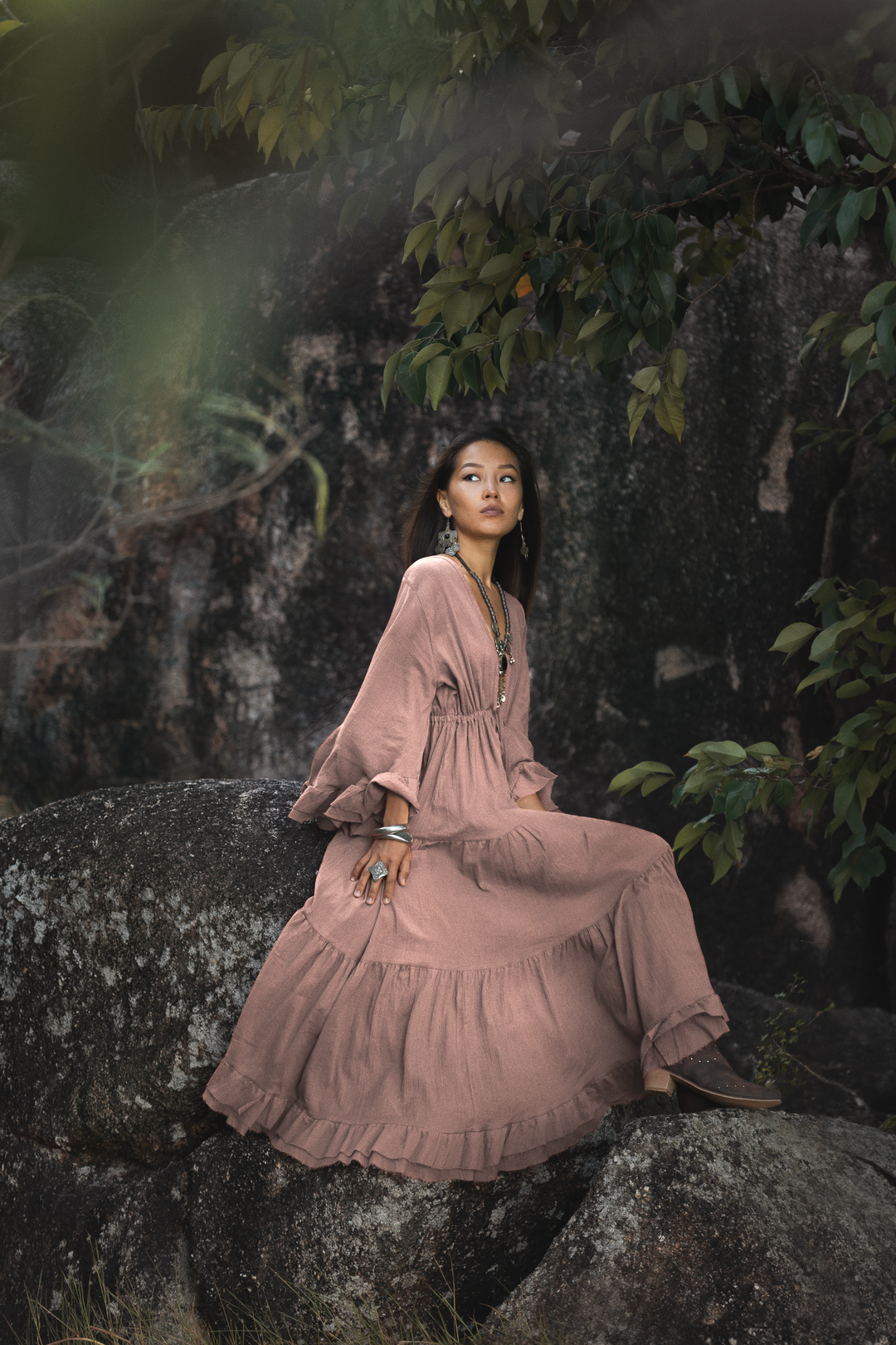 Woman in a pink dress sitting on a rock with a natural background