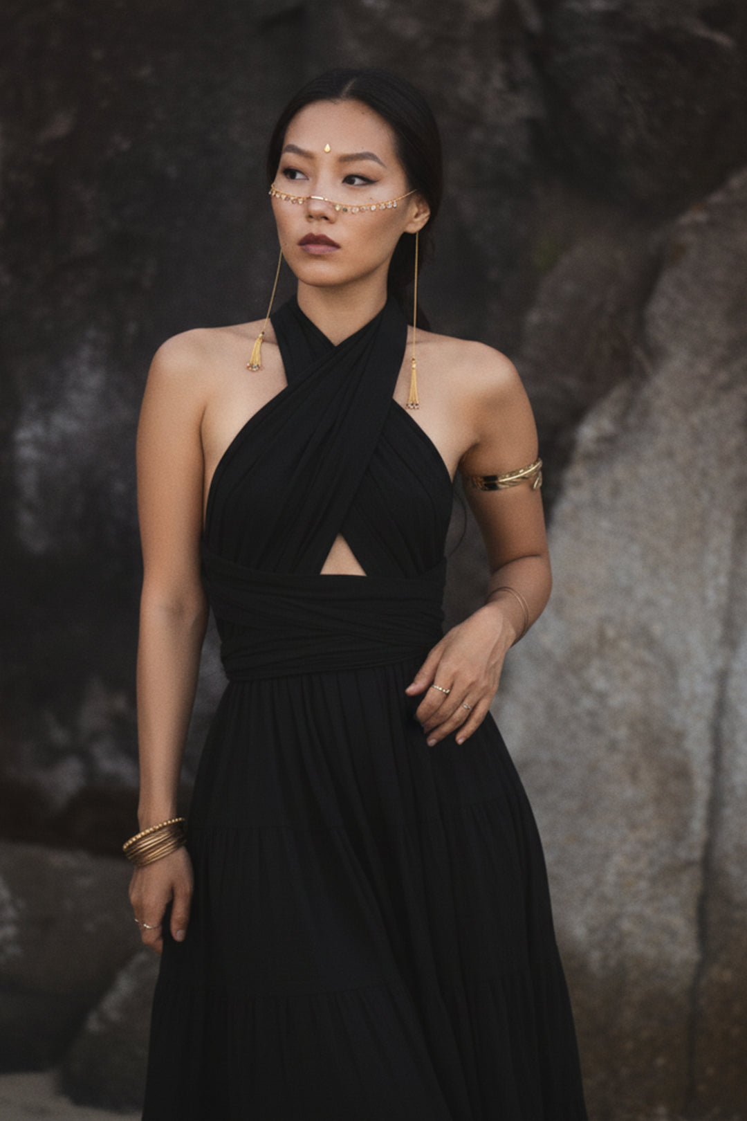 Woman wearing a black dress with gold jewelry against a dark background