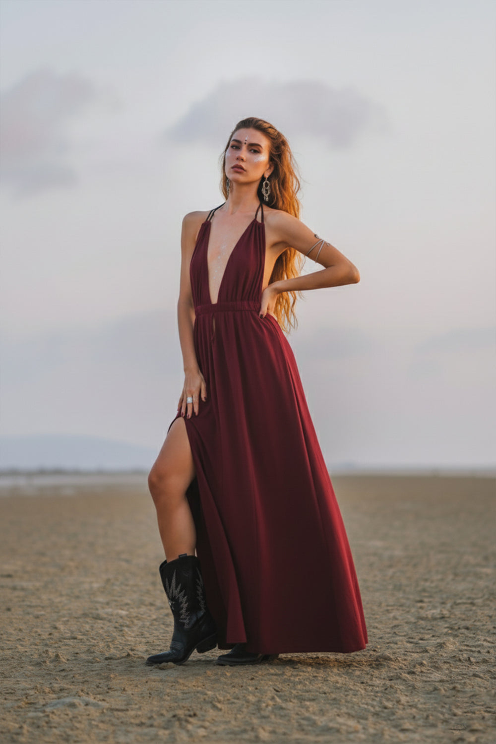 Woman in a burgundy dress with a high slit standing on a beach.