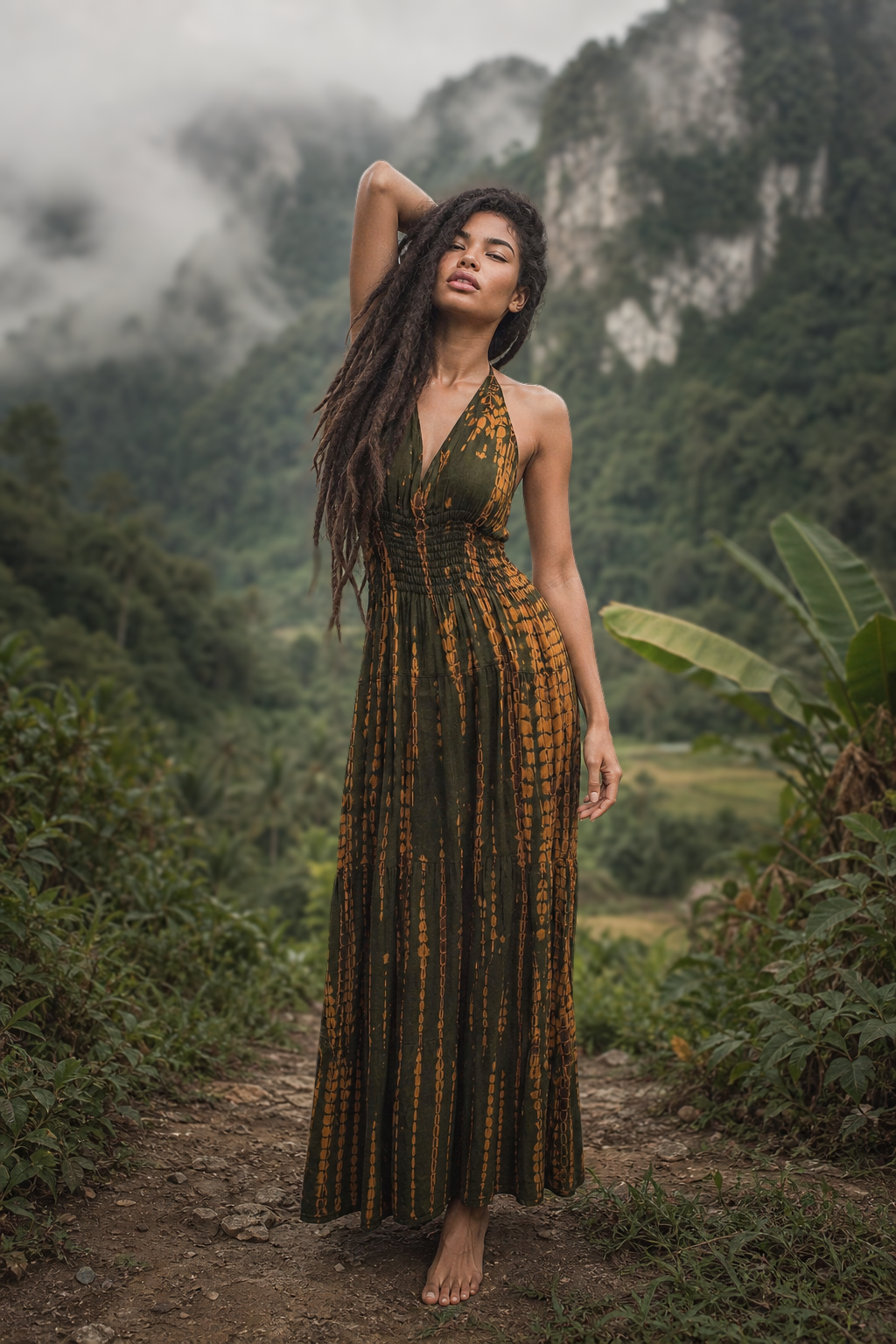 Woman in a green and brown patterned dress standing in a lush, mountainous forest.