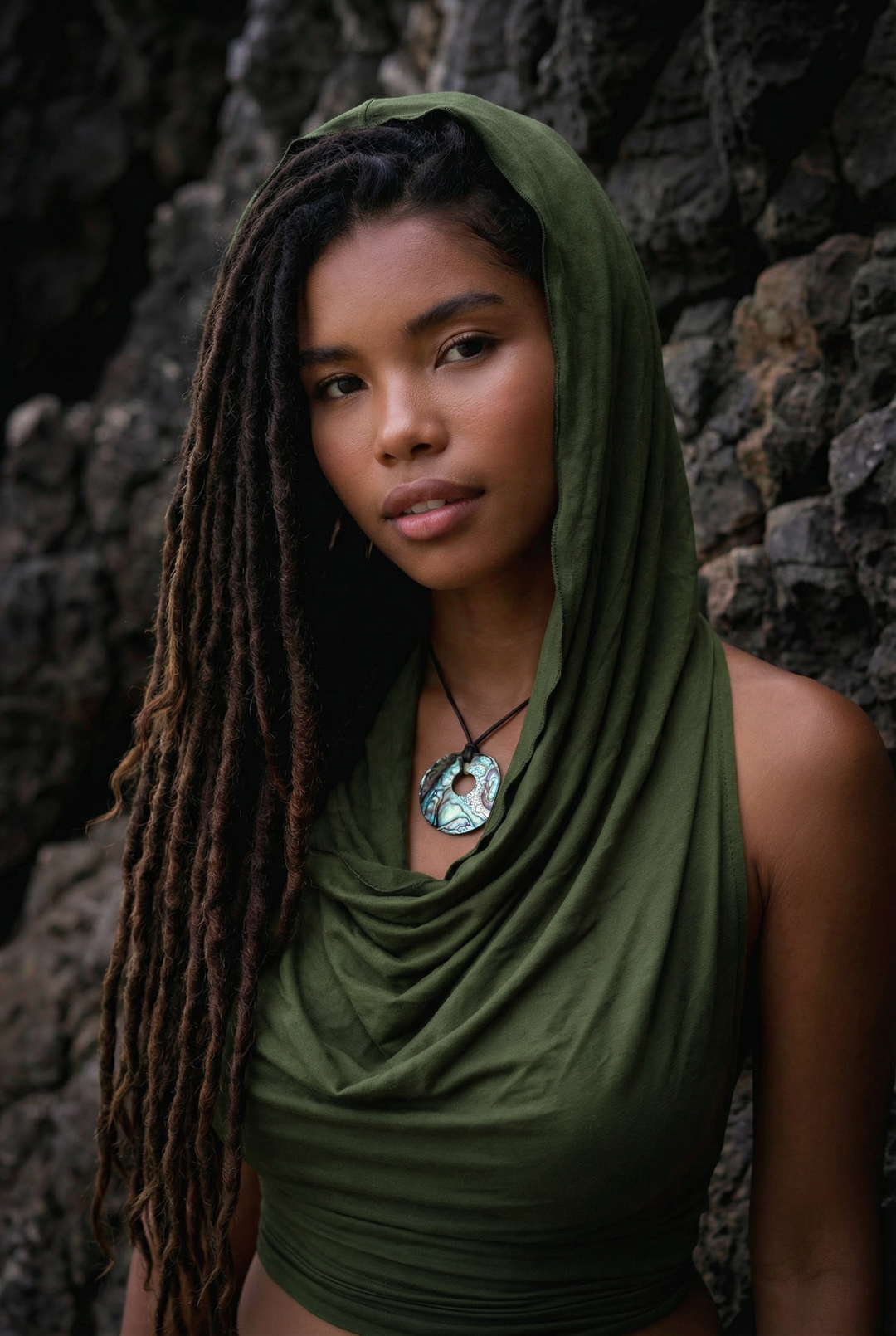 Woman wearing a green headscarf and top against a stone wall
