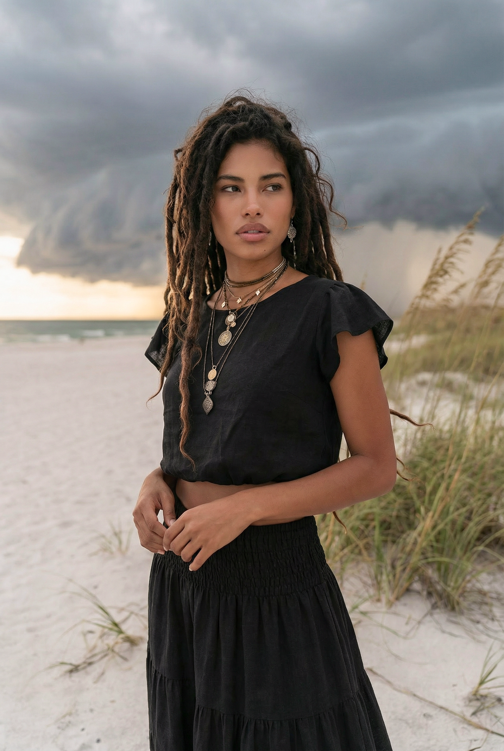 Woman in a black dress standing on a beach with stormy sky in the background