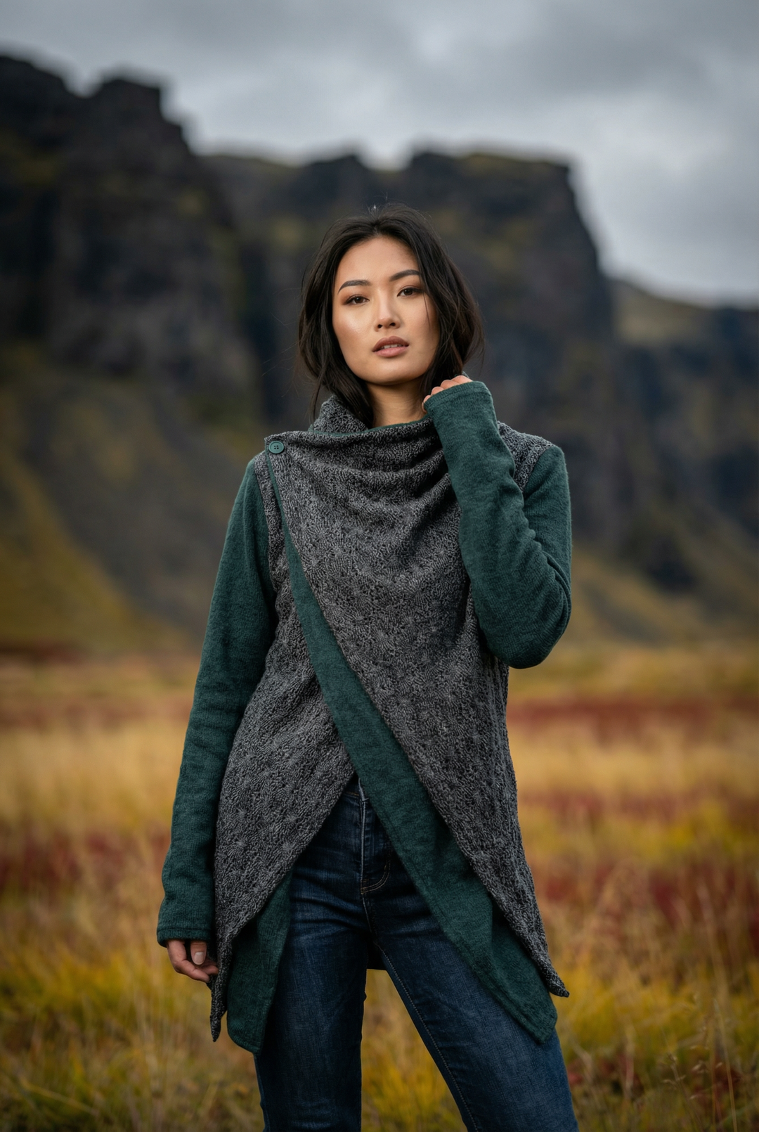 Woman wearing a green and gray coat standing in a field with mountains in the background