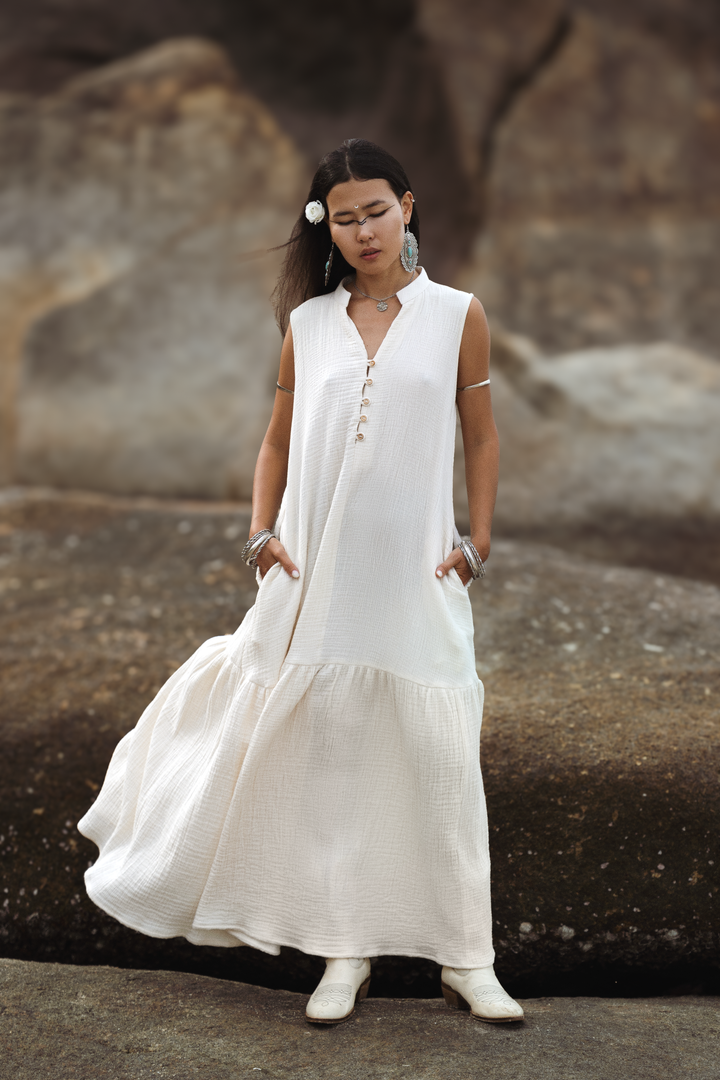 Woman wearing a white sleeveless dress standing against a rocky background