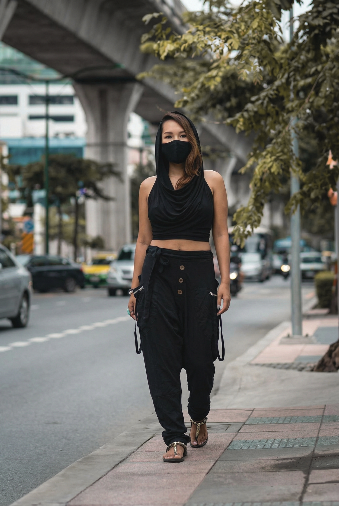 Woman in black outfit and mask walking on a city street