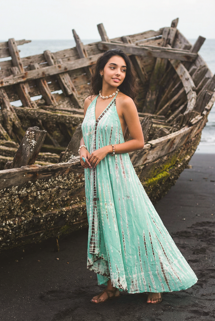 Woman in a light green dress standing in front of a sunken ship on a beach.