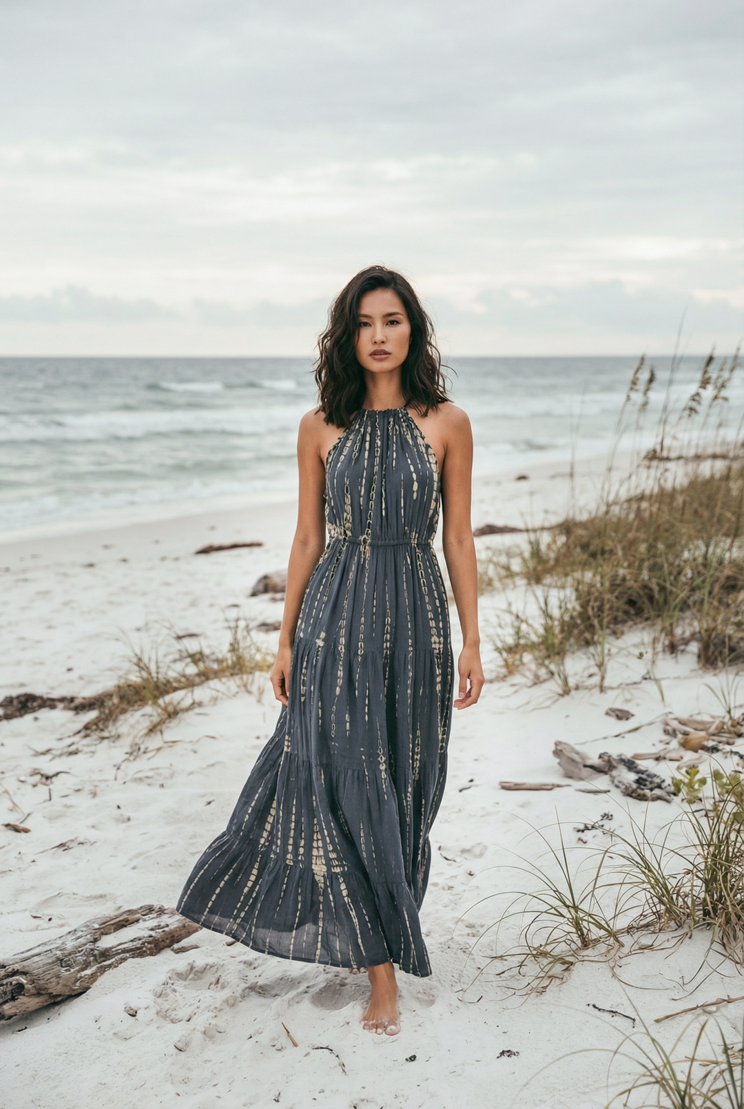 Woman in a long dress standing on a beach with ocean and sky in the background