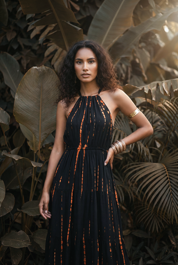 Woman in a black dress with orange accents standing among tropical plants