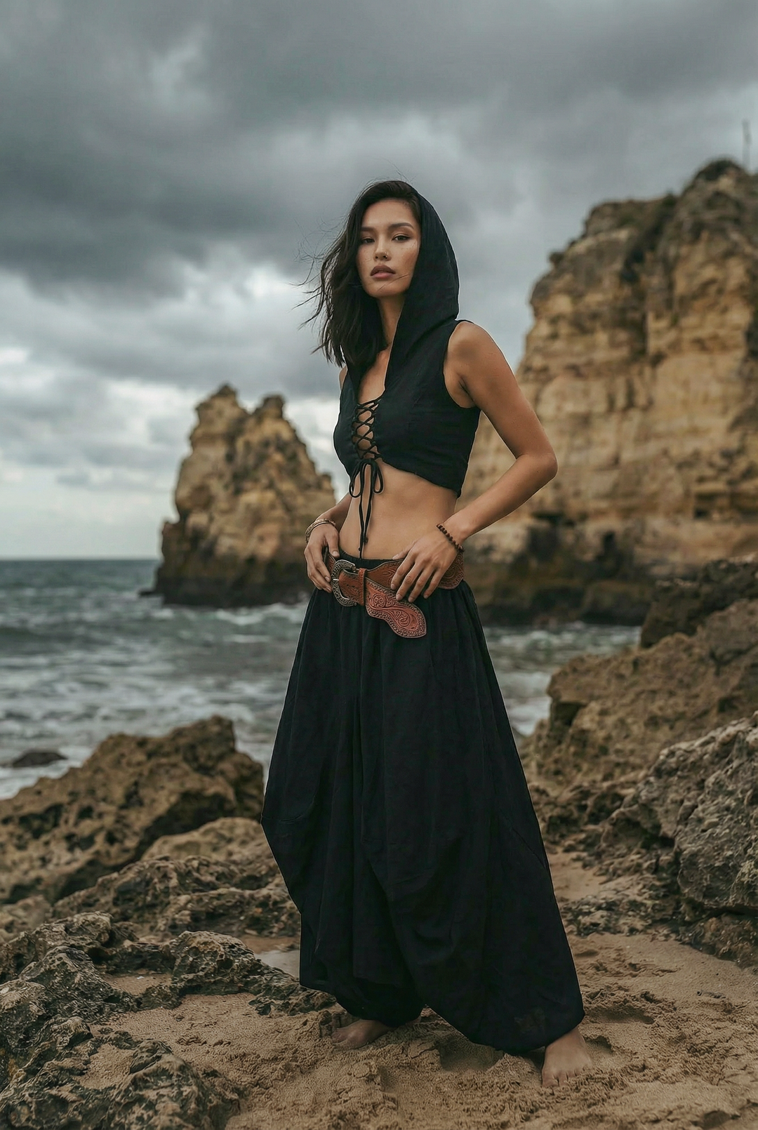 Woman in a black outfit standing on rocky beach with ocean and cliffs in the background