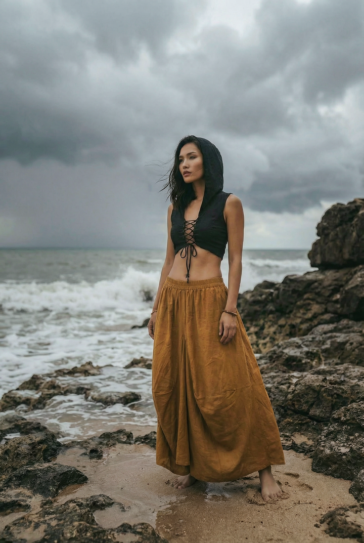 Woman in a black top and long mustard skirt standing on rocky beach with stormy sky