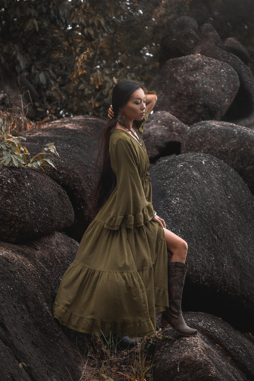 Woman in a long green dress and brown boots sitting on large rocks in a natural setting