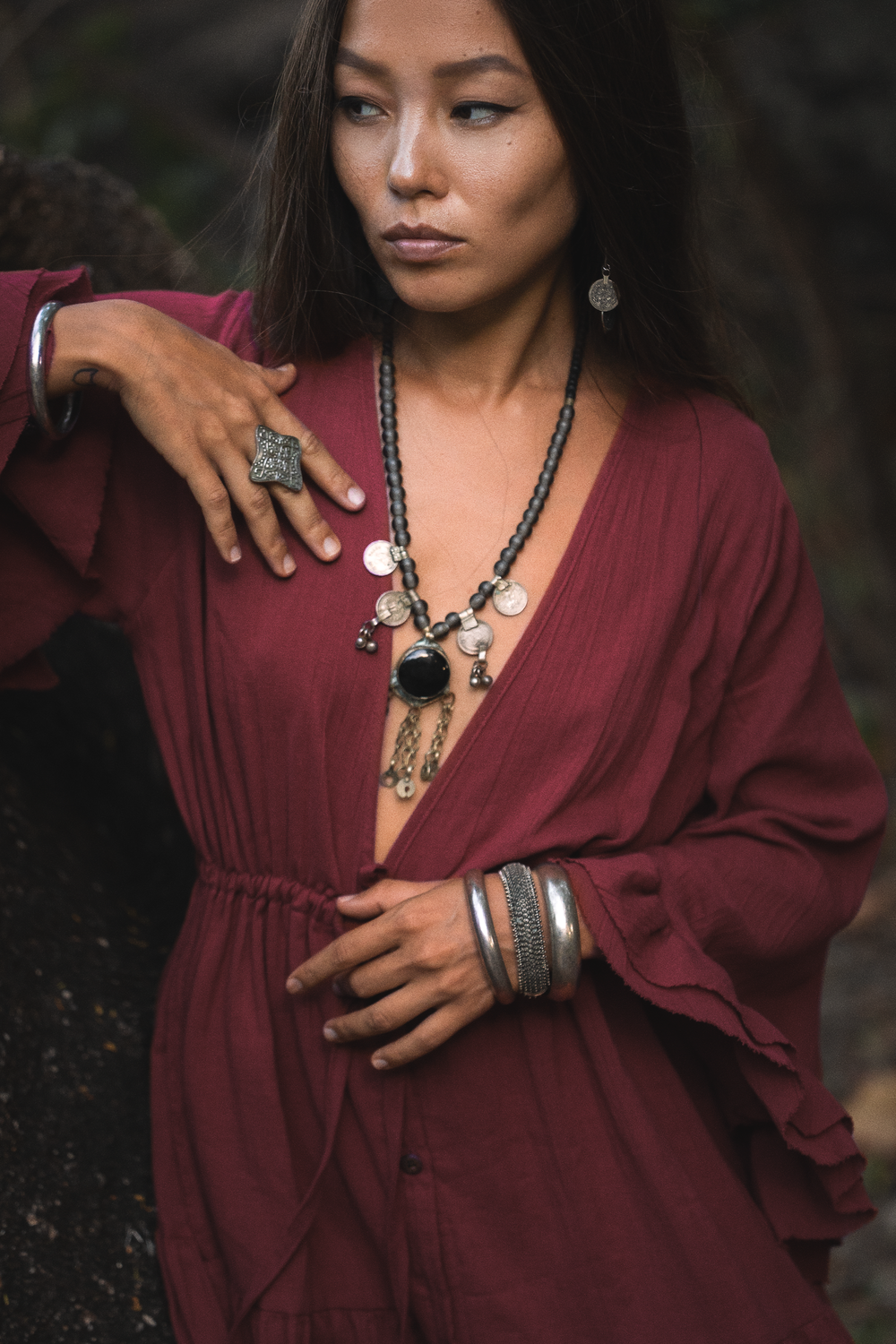 Woman in a burgundy dress with jewelry against a dark background