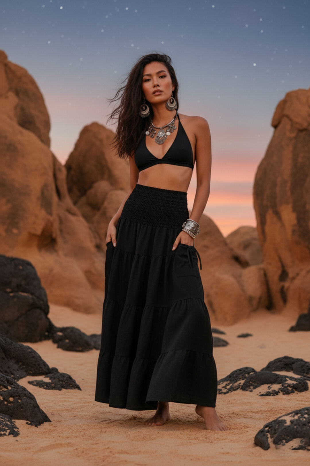 Woman in black outfit standing in a desert landscape with rocky formations and a sunset sky.